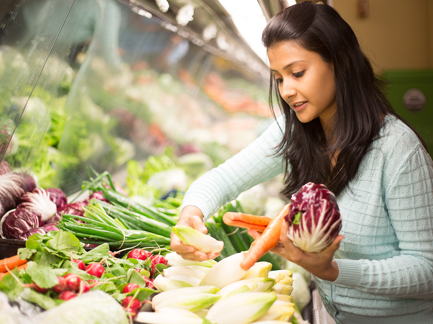 A woman picking out vegetables from the vegetable aisle in a grocery store