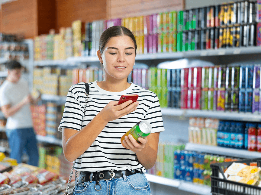 Woman using her phone while holding a drink in the store