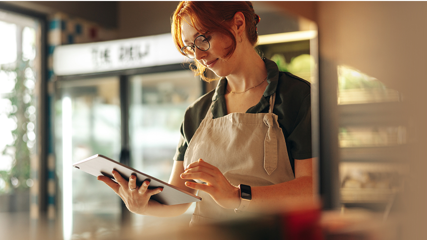 A woman working at a small grocery store uses a tablet