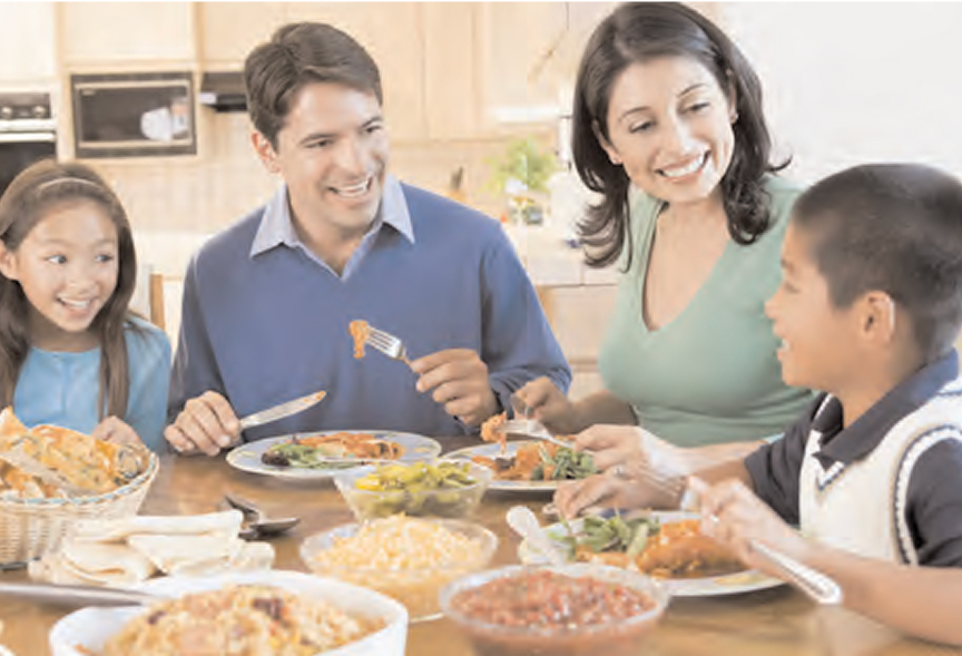 A family of four, including two adults and two children, sitting around a kitchen table enjoying a meal together.
