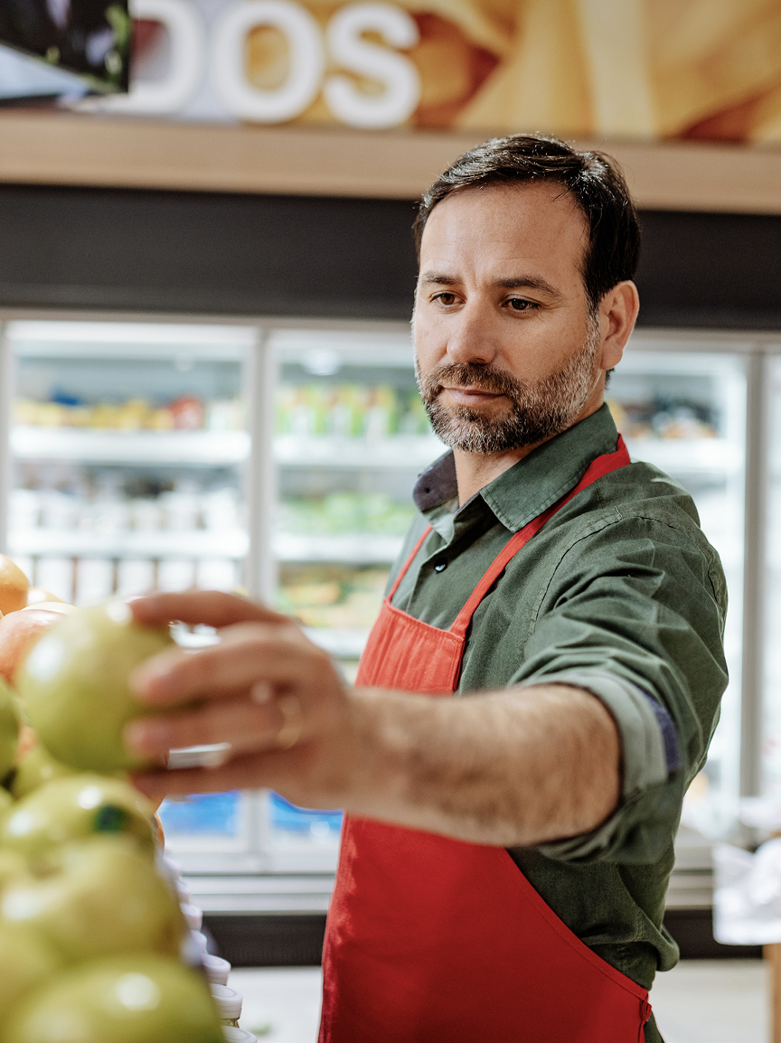 Grocery store employee placing an apple onto a produce display in a grocery store.