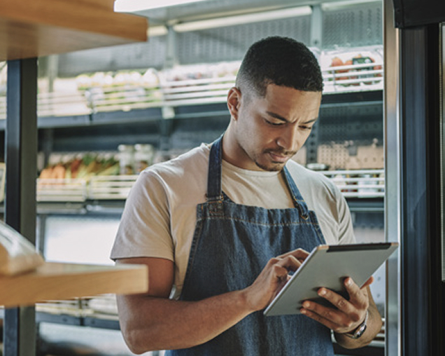 Grocery store employee using a tablet in front of a refrigerated produce section in a grocery store