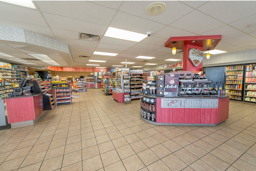 Wide view of a clean and brightly lit Loaf 'N Jug convenience store interior. The store is uncluttered, with shelves of fruit displayed beside the sales counter.